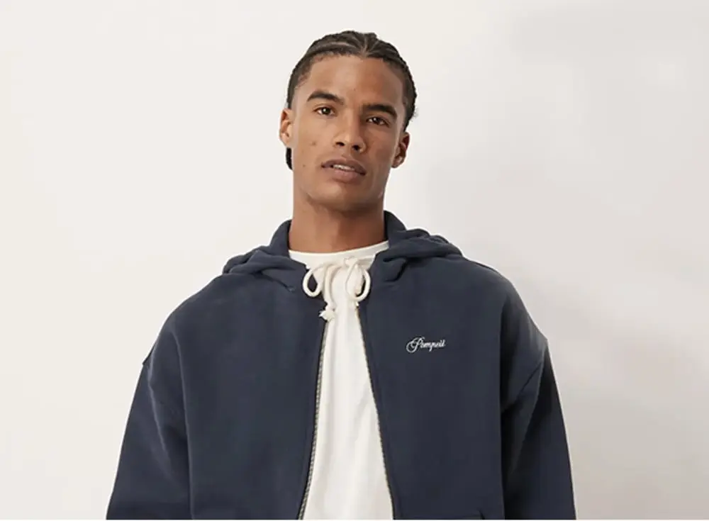 Un homme porte un sweat-shirt bleu ASOS avec capuche, debout devant un fond clair