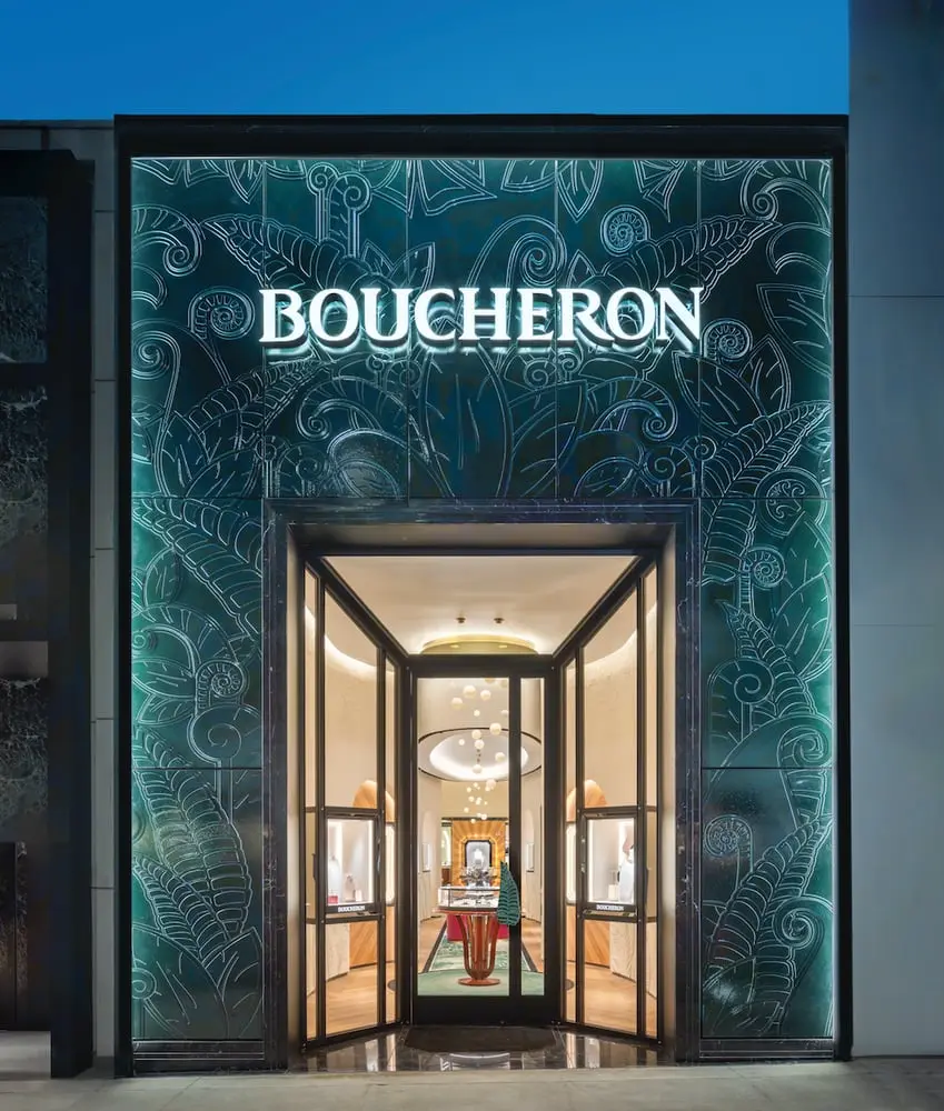 Façade d'une boutique Boucheron ornée de motifs élégants, éclairée à l'entrée avec des vitrines intérieures visibles.