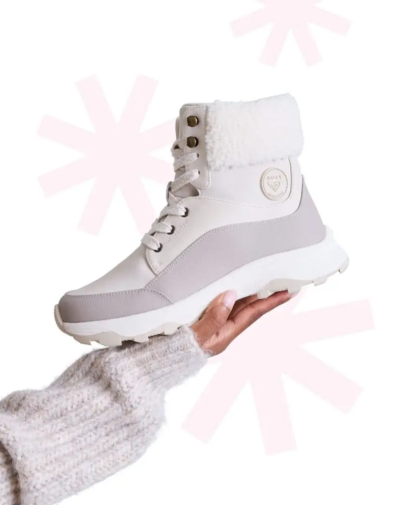 Main tenant une botte blanche à motif étoilé de Designer Brands, fond blanc et rose pale