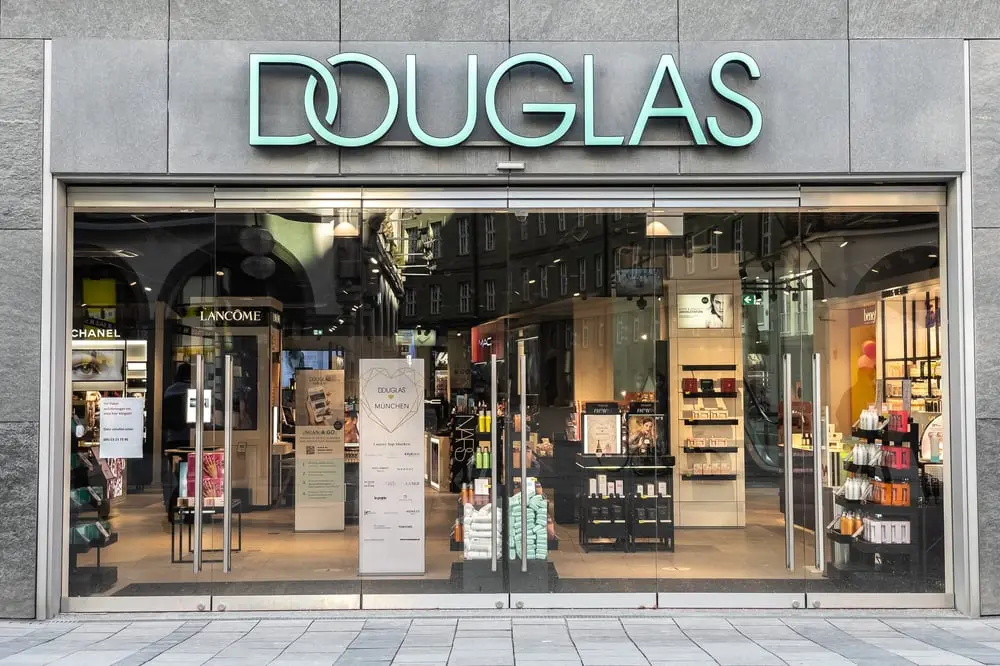 Entrée d'un magasin Douglas avec enseigne lumineuse, vitrines affichant divers produits cosmétiques à l'intérieur