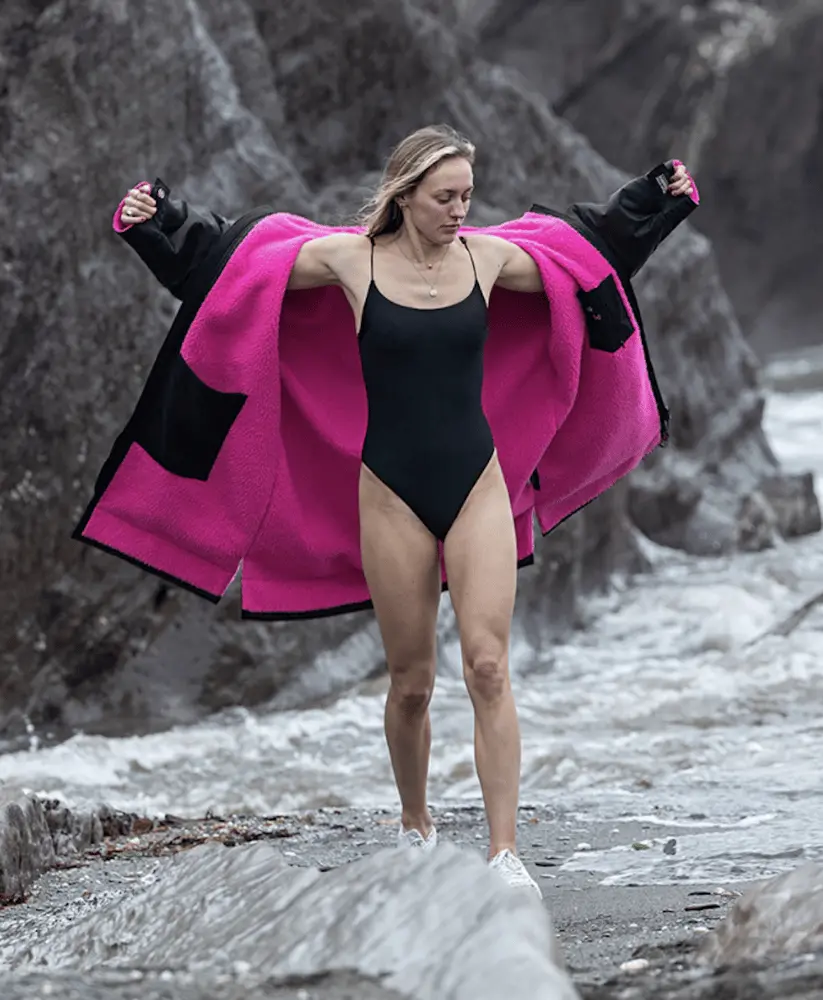 Femme en maillot de bain portant un peignoir Dryrobe noir et rose près de rochers en bord de mer