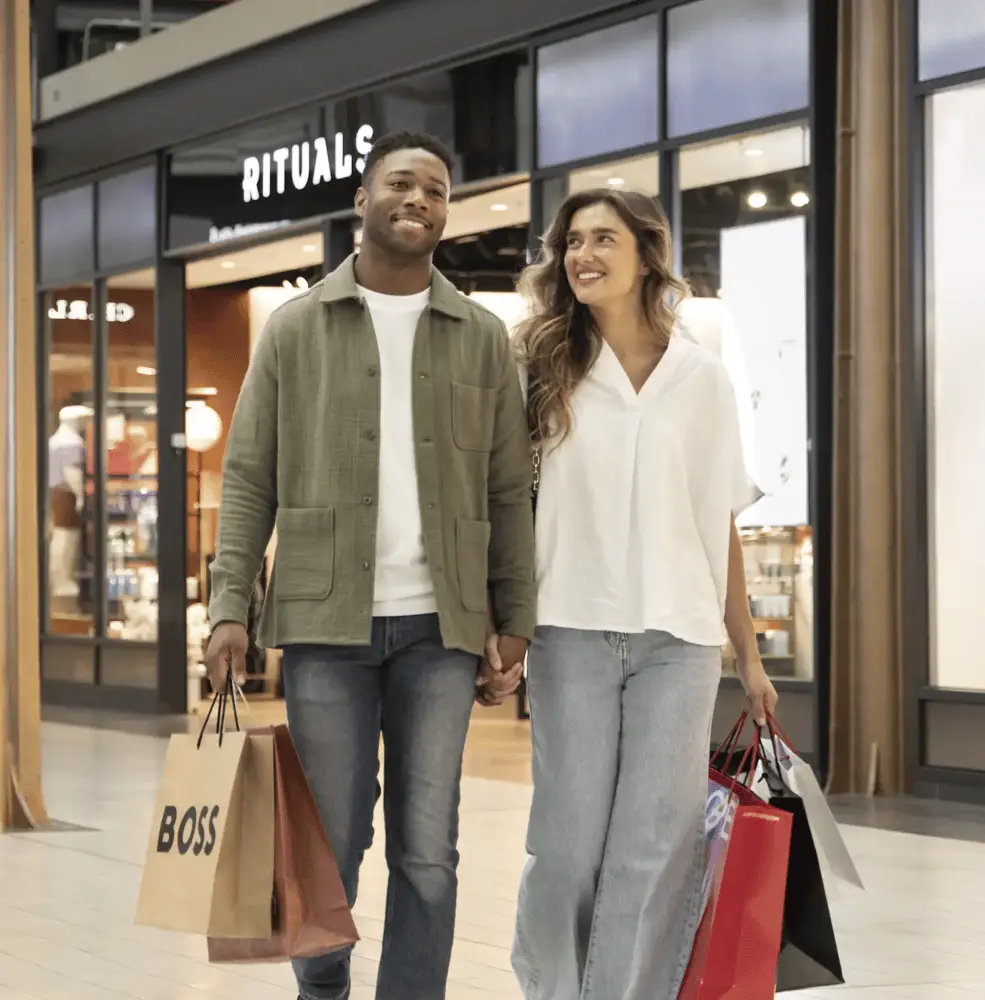Un couple marche dans le Swindon Designer Outlet en portant des sacs de shopping devant la boutique Rituals