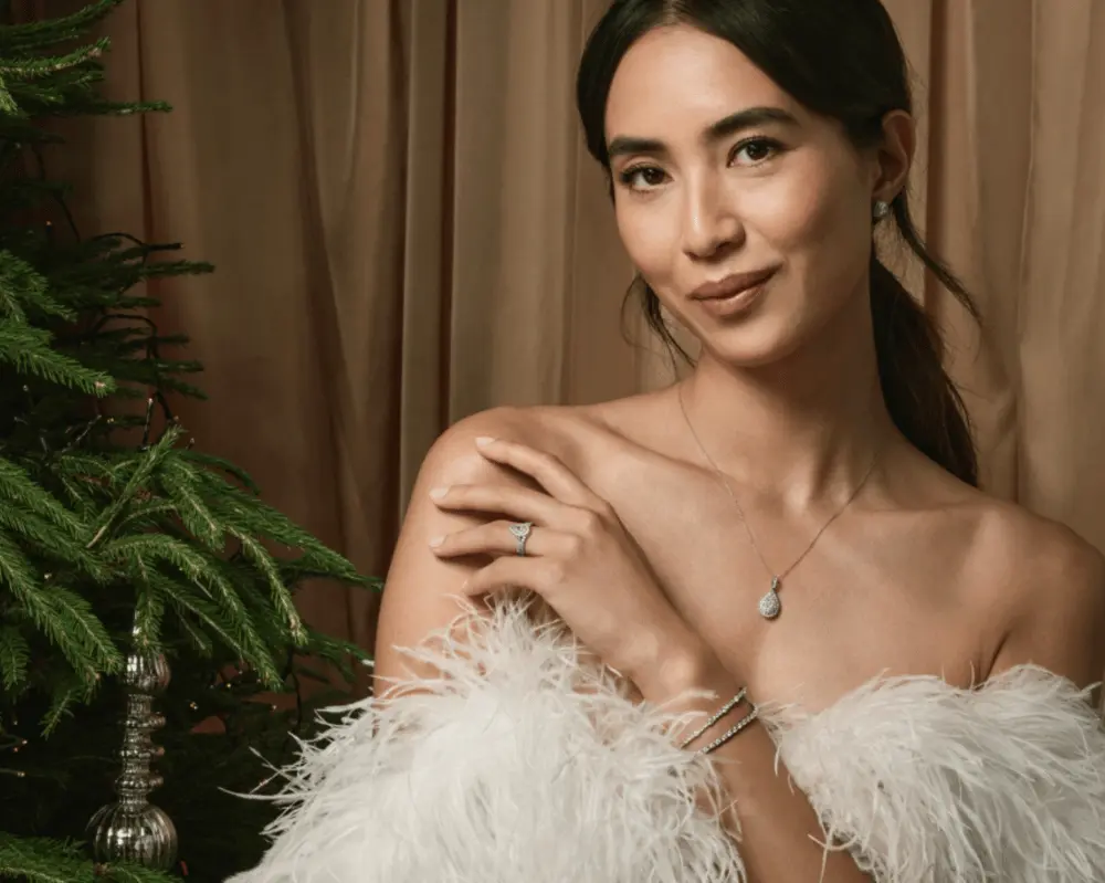 Femme élégante portant des bijoux près d'un sapin, posant avec un collier et des boucles d'oreilles Signet