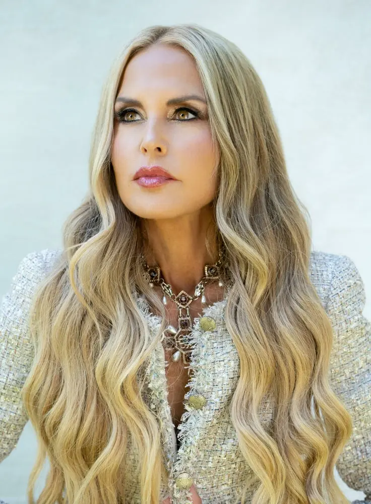 Femme aux longs cheveux blonds portant un collier et une veste texturée, regardant vers la gauche