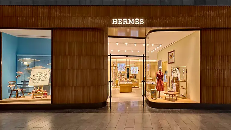 Vitrine d'une boutique Hermès illuminée, affichant des articles de luxe tels que vêtements et accessoires
