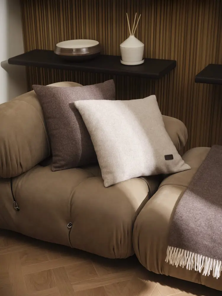 Coussins gris et taupe sur canapé en velours beige dans un intérieur moderne, soulignant la collection Habita de Herno