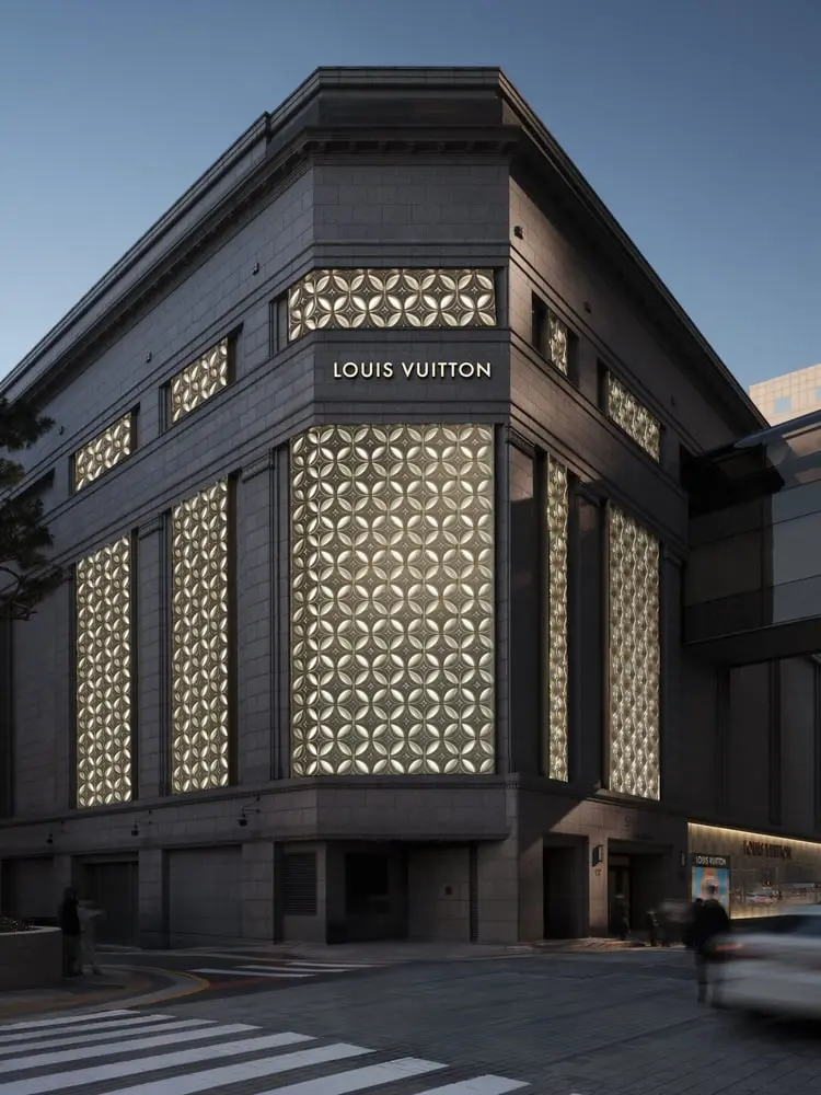 Façade illuminée du magasin Louis Vuitton avec motifs géométriques, angle de rue au crépuscule.