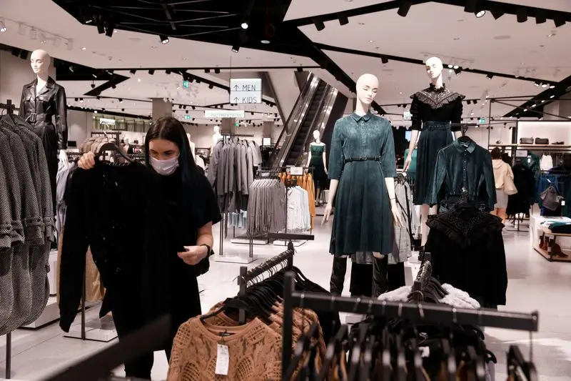 Une cliente masquée parcourt un magasin LPP bien éclairé, entourée de mannequins vêtus de robes élégantes