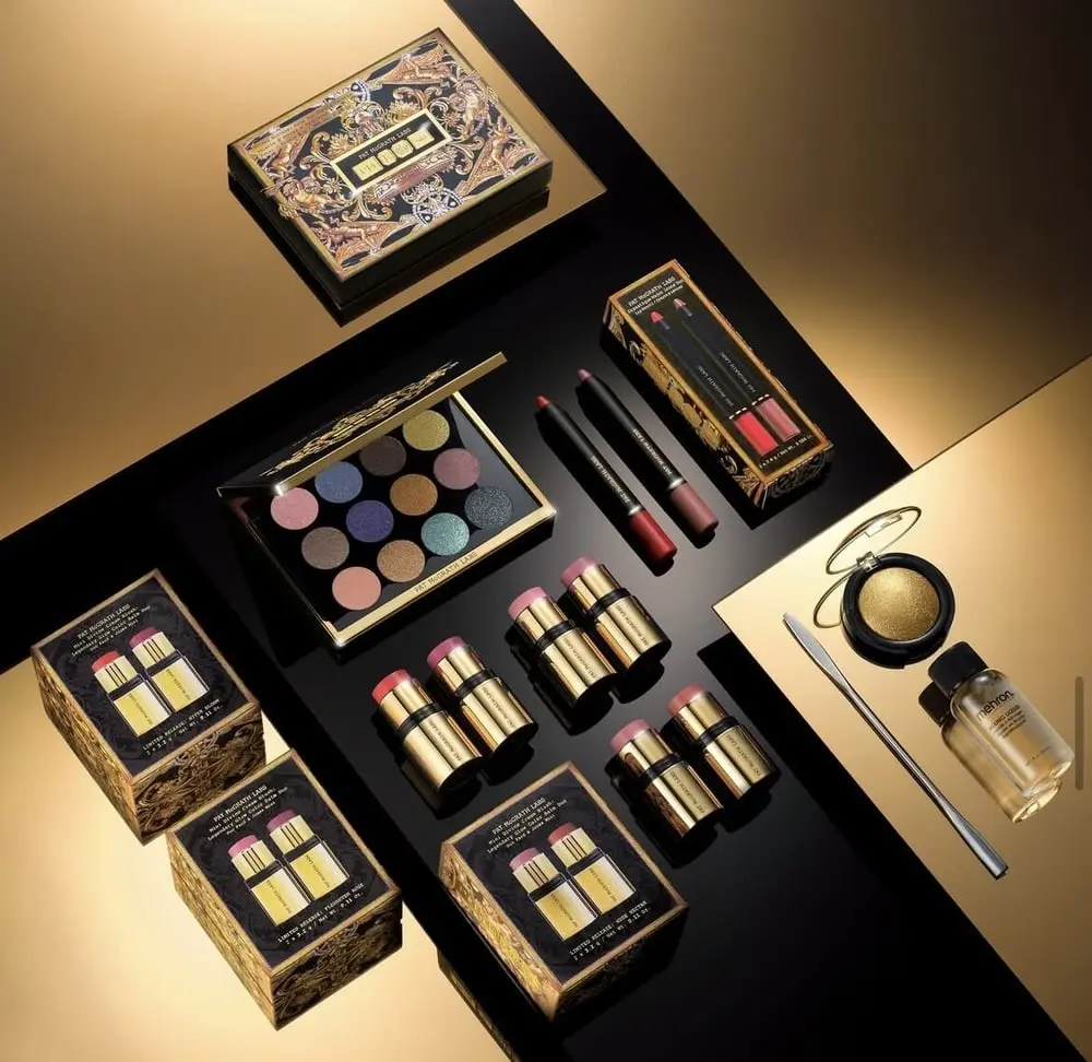 Produits de maquillage Pat McGrath Labs incluant palettes, rouges à lèvres et poudres disposés sur fond doré et noir