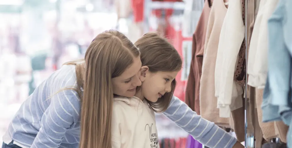 Deux jeunes filles souriantes choisissent des vêtements dans un magasin Pepco.