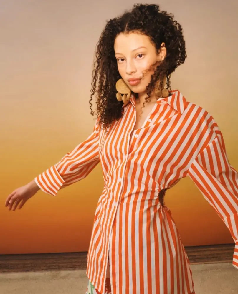 Personne en chemise à rayures rouges et blanches de Rent the Runway posant devant un fond de coucher de soleil.