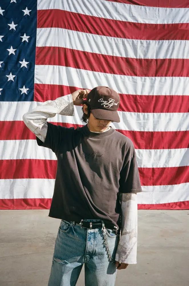 Un modèle porte une casquette Represent devant un grand drapeau américain en arrière-plan
