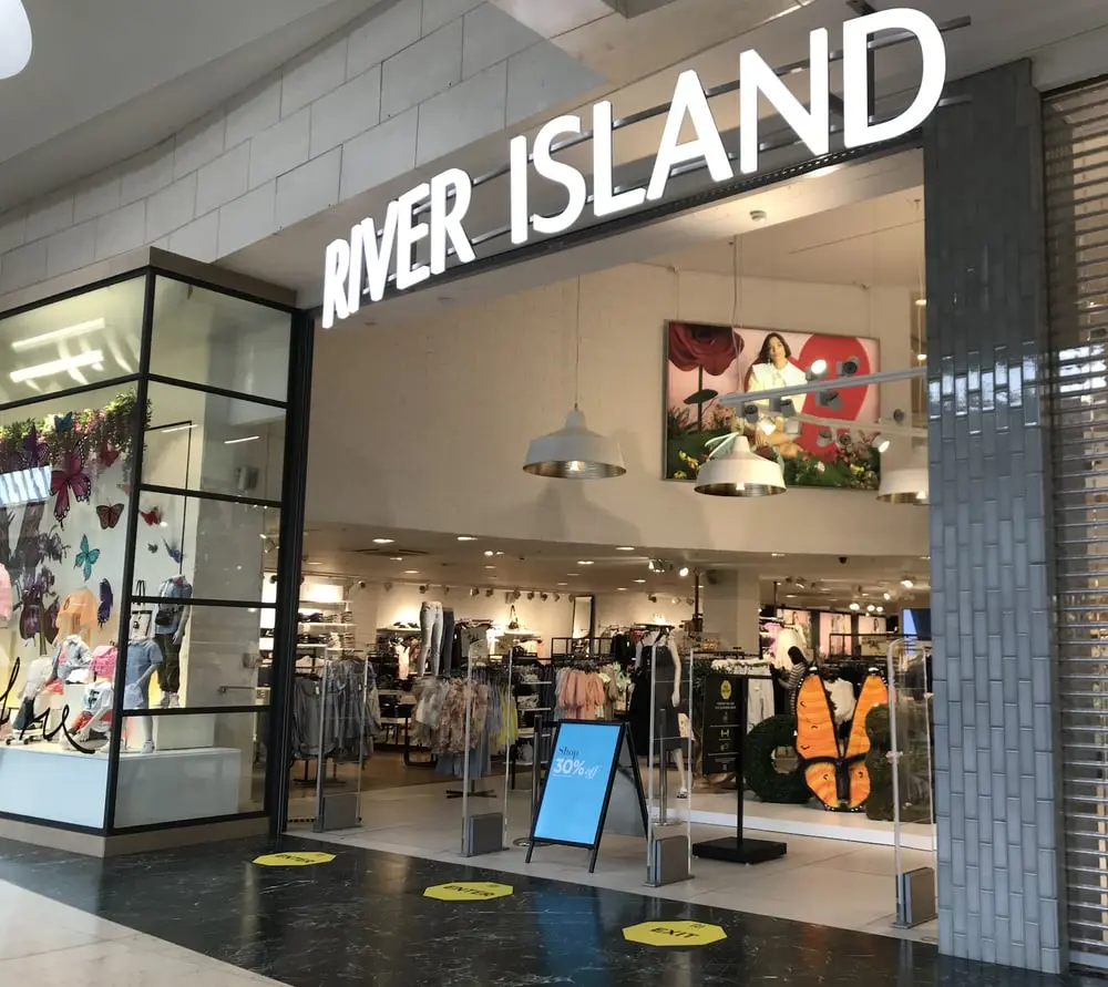 Magasin River Island dans un centre commercial avec des vêtements exposés et panneau de réduction de 30%