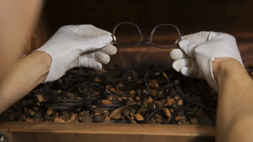 Gants blancs manipulant des lunettes au-dessus d'une boîte en bois remplie de montures de lunettes Safilo