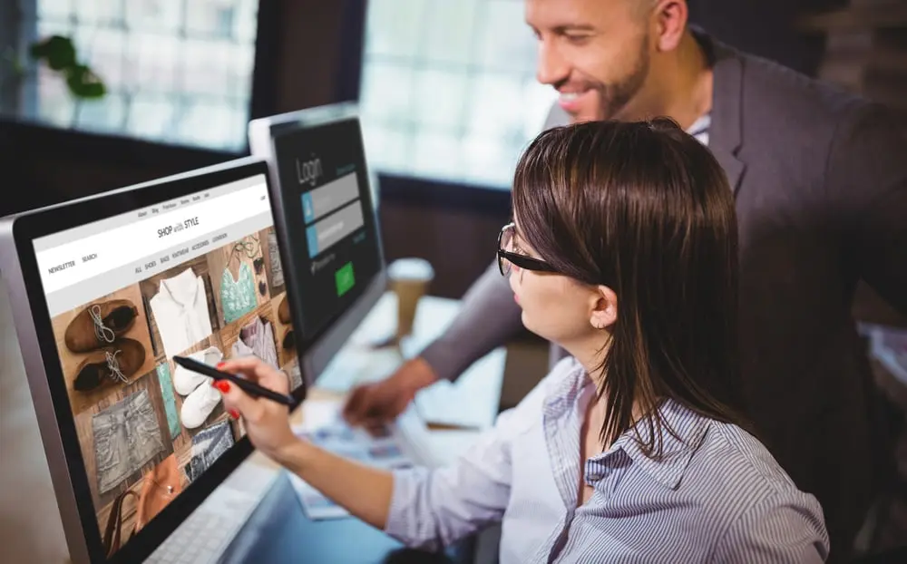 Un homme et une femme analysent un site web de mode sur un écran d'ordinateur dans un bureau lumineux.
