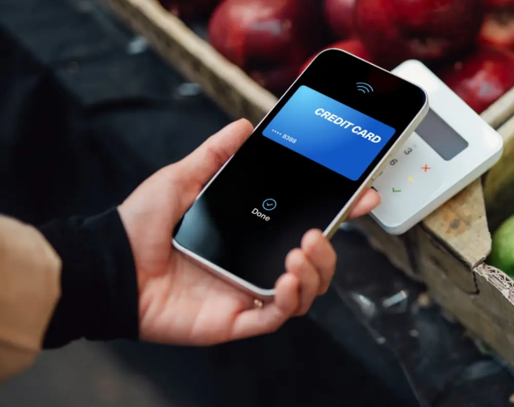 Transaction mobile avec carte de crédit affichée sur un téléphone près d'un terminal, symbolisant les taux d'intérêt élevés