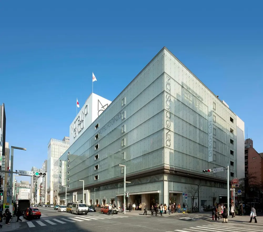 Le grand magasin Matsuya Ginza à Tokyo sous un ciel bleu avec des passants et des voitures en mouvement