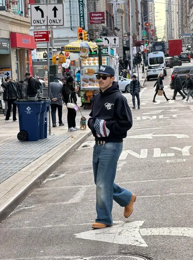 Un homme portant du streetwear marche dans une rue animée de New York, devant un stand de nourriture