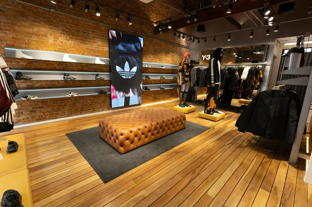 Intérieur d'une boutique Adidas avec canapés en cuir et étagères exposant des chaussures et des vêtements sportifs.