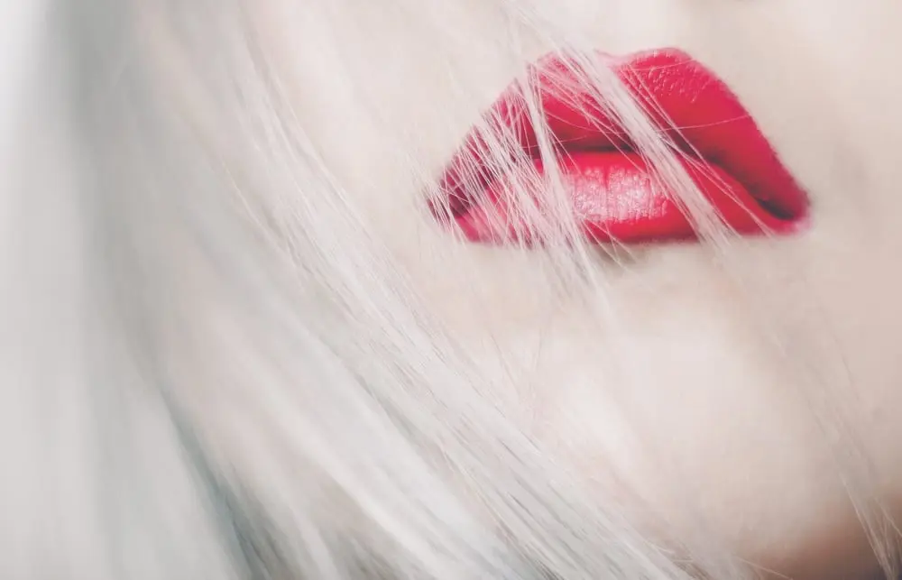 Lèvres rouge vif parmi des mèches de cheveux blancs, évoquant une touche de beauté audacieuse et accessible