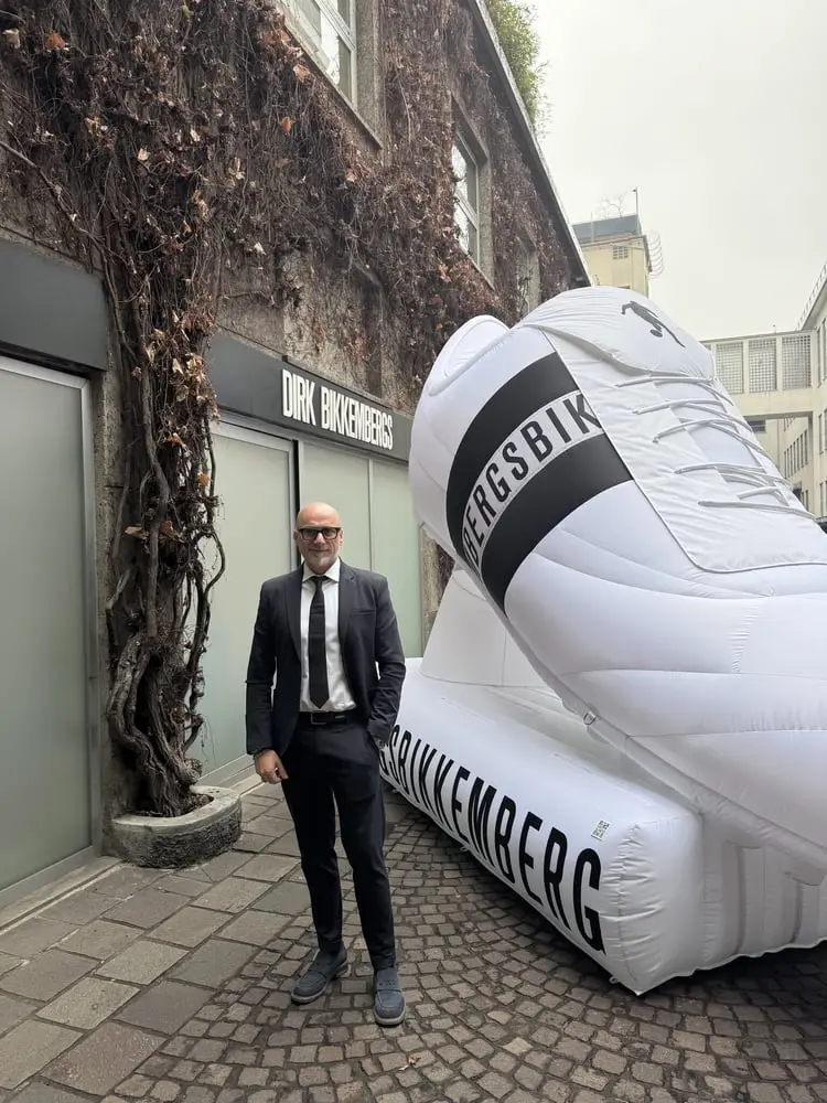 Un homme en costume debout devant un magasin Dirk Bikkembergs avec une grande chaussure gonflable blanche.