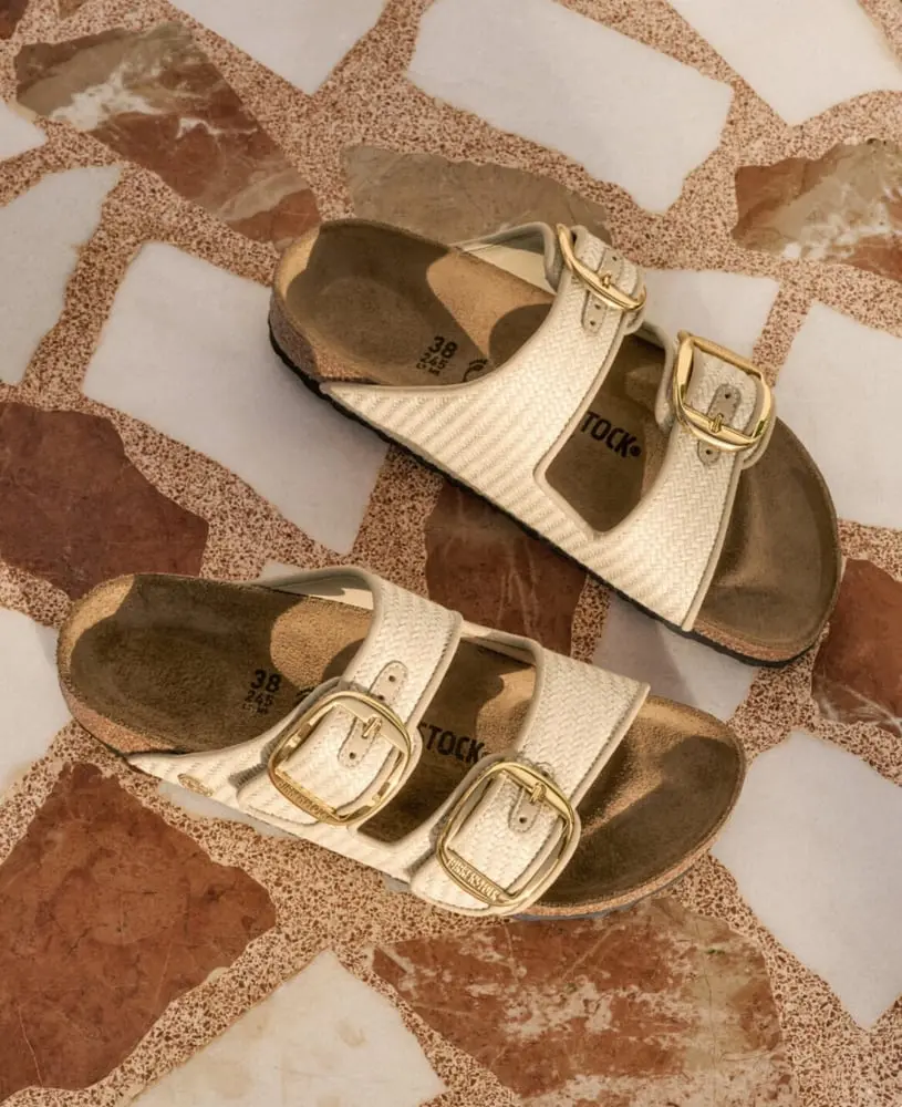 Sandales Birkenstock beiges avec boucles dorées posées sur un sol aux motifs géométriques