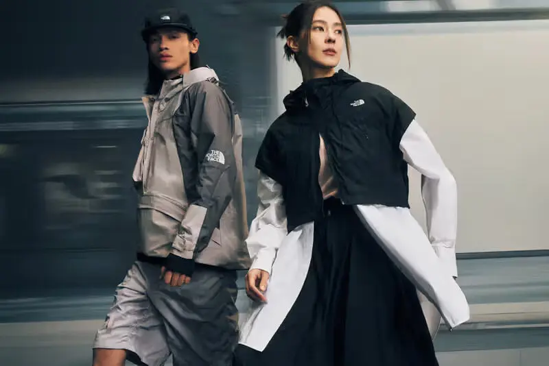 Deux mannequins arborent des vêtements d'extérieur North Face, marchant dans un environnement urbain, en mouvement.