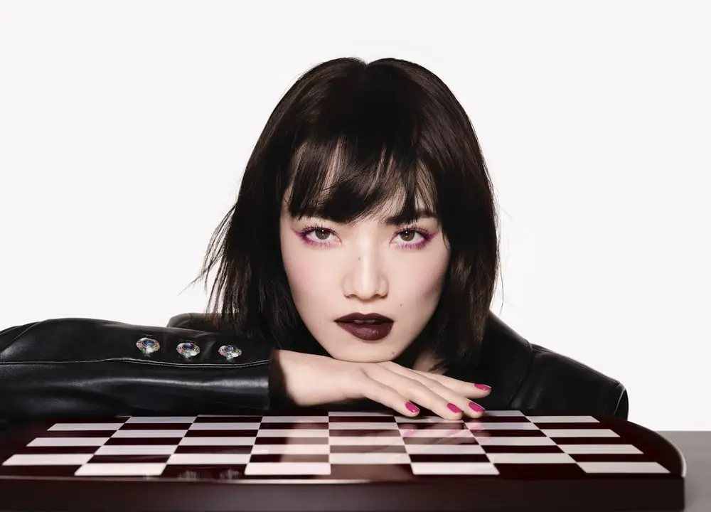 Personne au maquillage Chanel sombre et intense inspiré du Rouge Noir posant devant un échiquier.