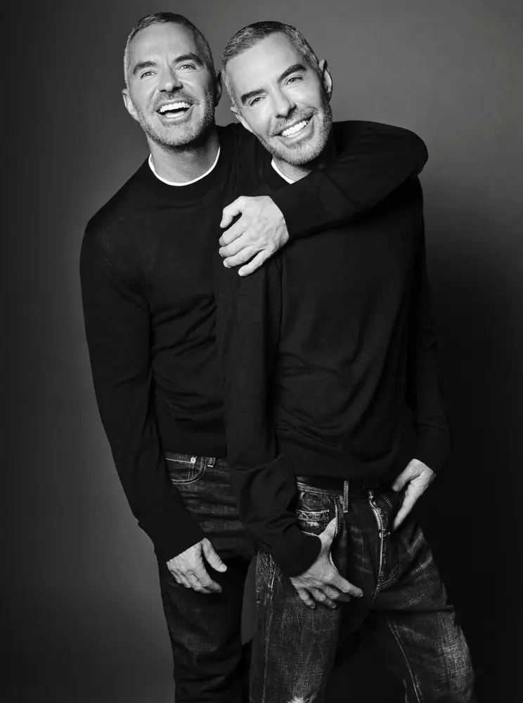 Deux hommes souriants en pulls noirs et jeans posent devant un fond gris, illustrant le style Dsquared2.