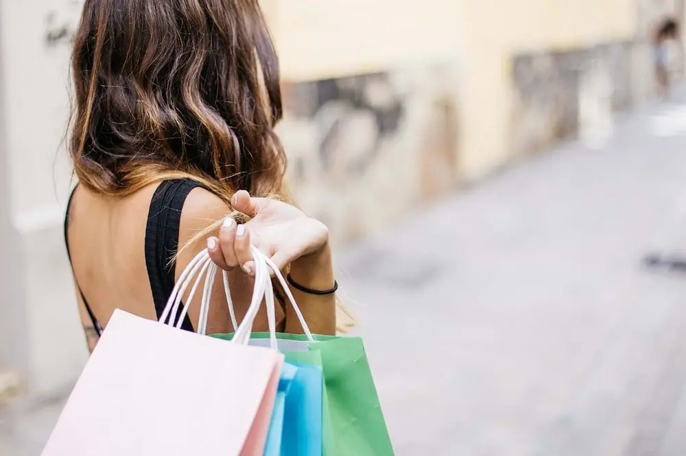 Une femme portant des sacs à provisions colorés marche dans une rue commerçante, illustrant l'univers de Farfetch