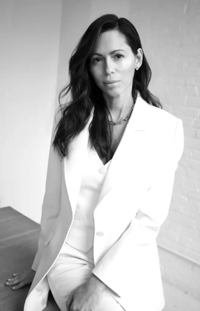 Une femme en costume blanc est assise dans un environnement épuré, associée à Gabriela Hearst