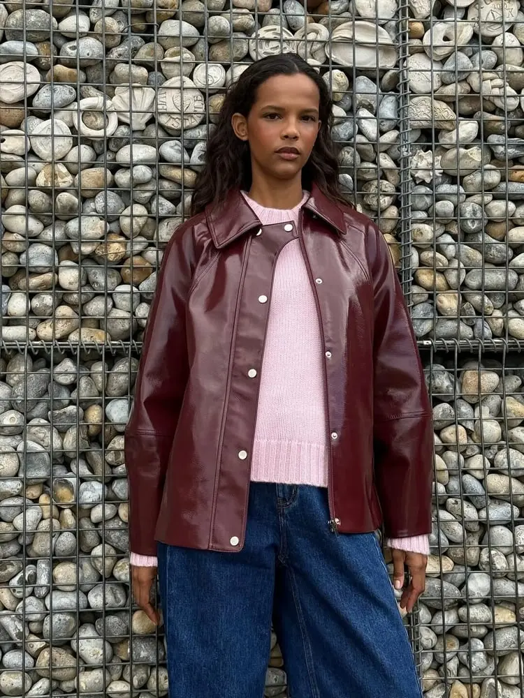 Personne portant une veste en cuir rouge et un pull rose devant un mur de pierres, symbolisant Hush Homewear.