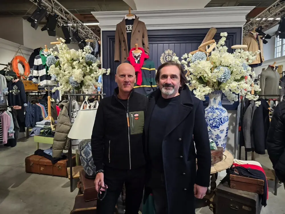 Deux hommes devant des vêtements et décorations dans un magasin, mettant en avant la marque britannique Belstaff