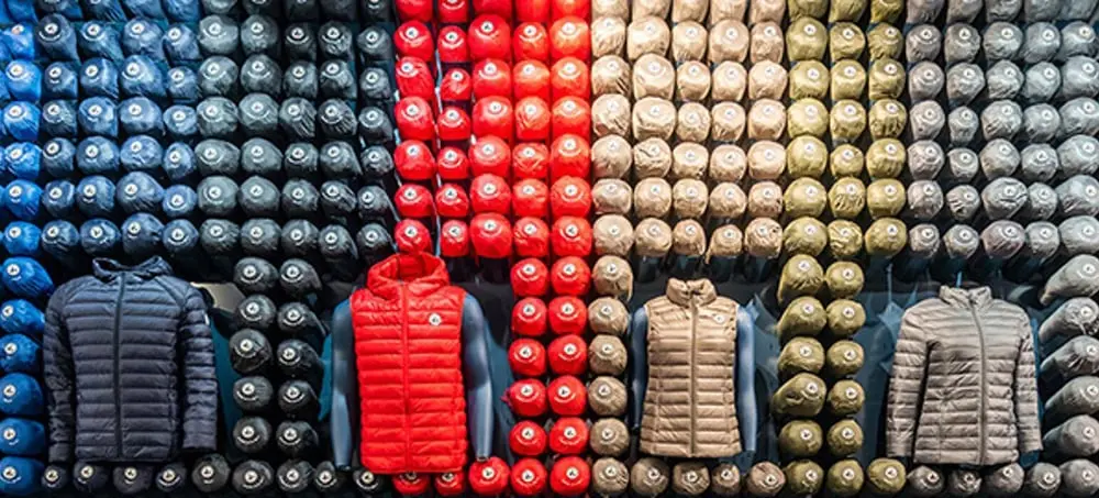 Doudounes JOTT exposées en magasin, alignées sur fond de rouleaux colorés bleu, rouge, beige et kaki