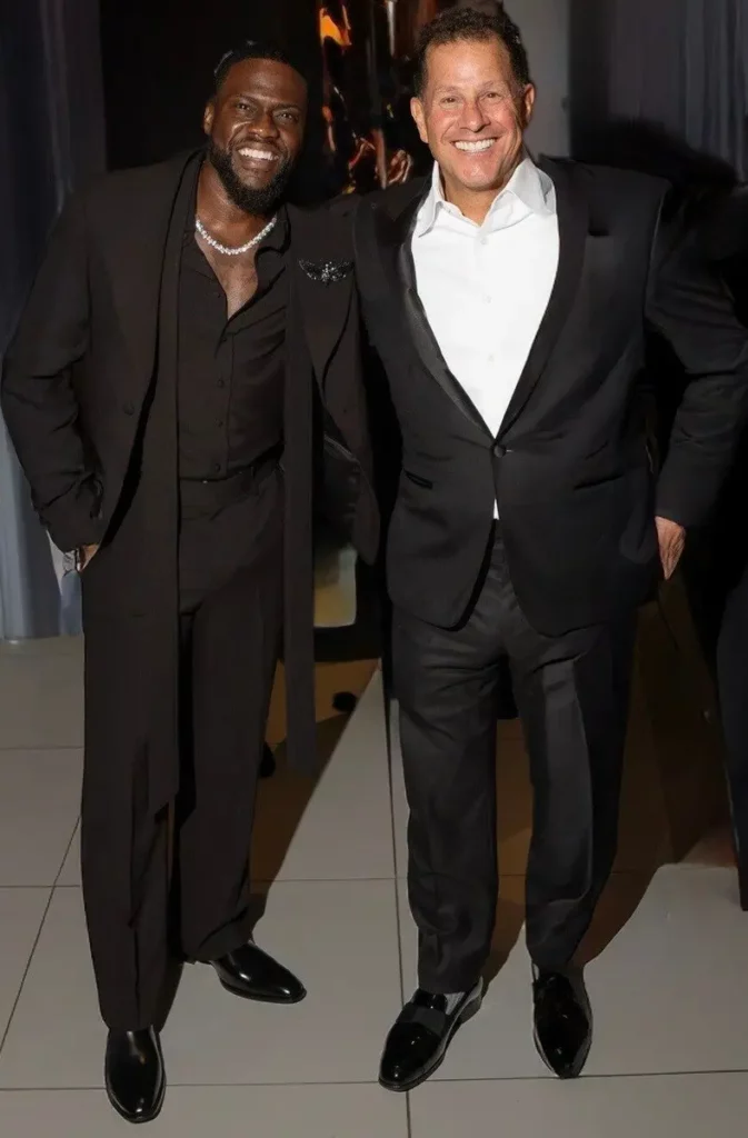 Deux hommes souriants en costumes formels lors d'un événement, Kevin Hart co-propriétaire chez Authentic Brands Group