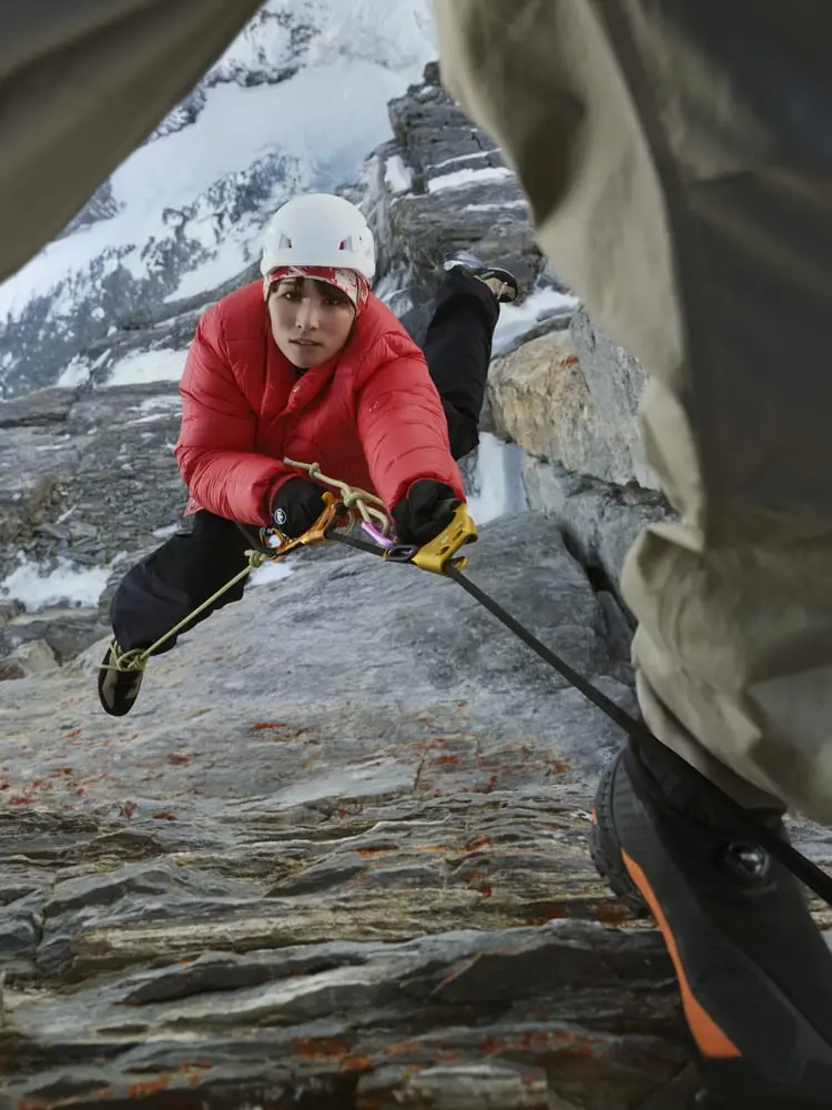 Alpiniste en veste Mammut rouge escaladant une paroi rocheuse enneigée avec détermination