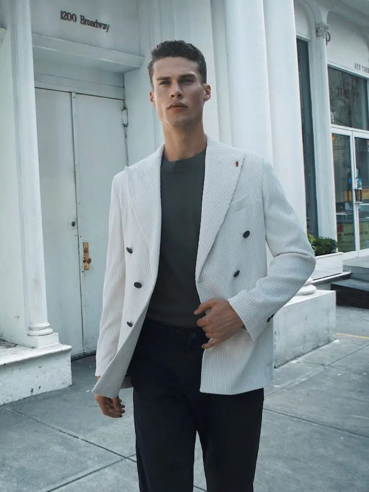 Un homme portant un élégant blazer blanc Mulish marche en ville devant un bâtiment.
