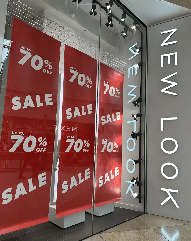 Affiches rouges annonçant jusqu'à 70 % de réduction chez New Look dans une vitrine de magasin moderne
