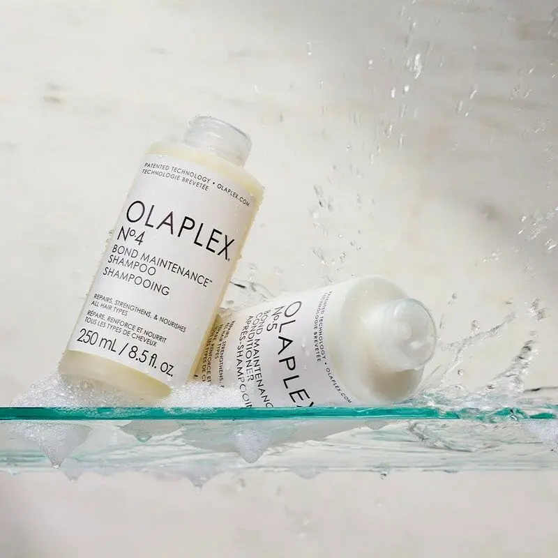 Deux bouteilles de shampooing Olaplex sur une surface mouillée, entourées d'éclaboussures d'eau.