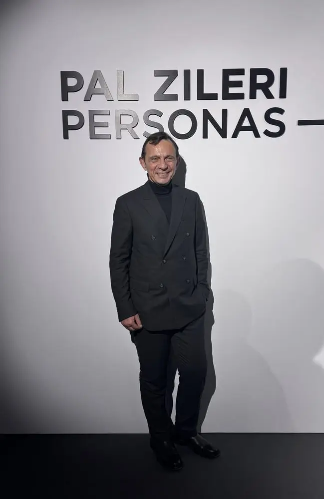 Une personne souriante en costume sombre pose devant un panneau Pal Zileri lors d'un événement de marque