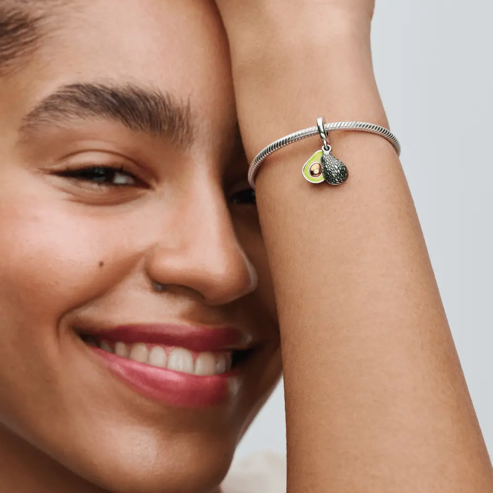 Une femme souriante porte un bracelet Pandora avec un pendentif en forme d'avocat.