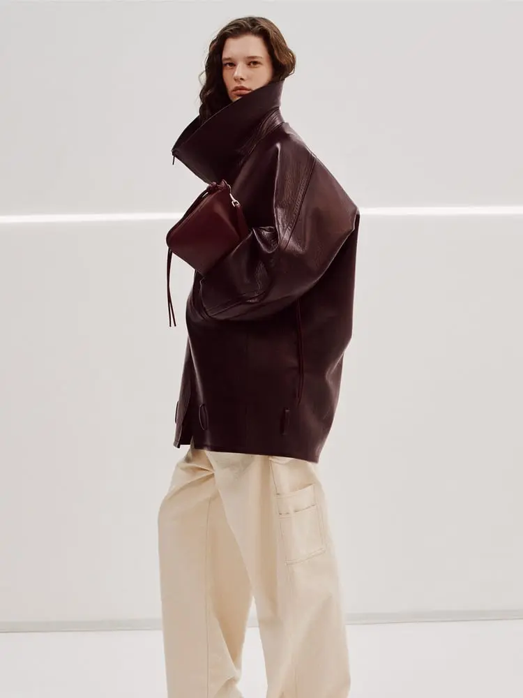 Personne en manteau en cuir sombre Phoebe Philo avec un sac assorti, debout sur un fond blanc épuré