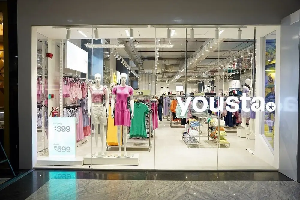 Façade vitrée d'un magasin de vêtements "Yousta" avec des mannequins portant des tenues colorées.