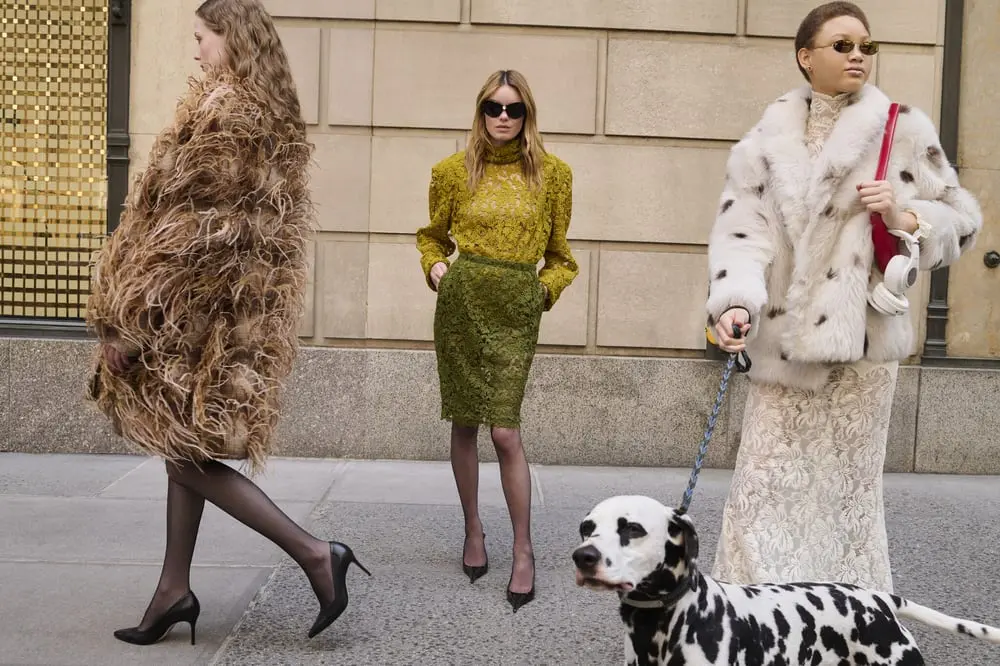 Trois femmes élégantes marchent en ville, l'une tenant un dalmatien, illustrant la mode et le luxe associés à Saks Global