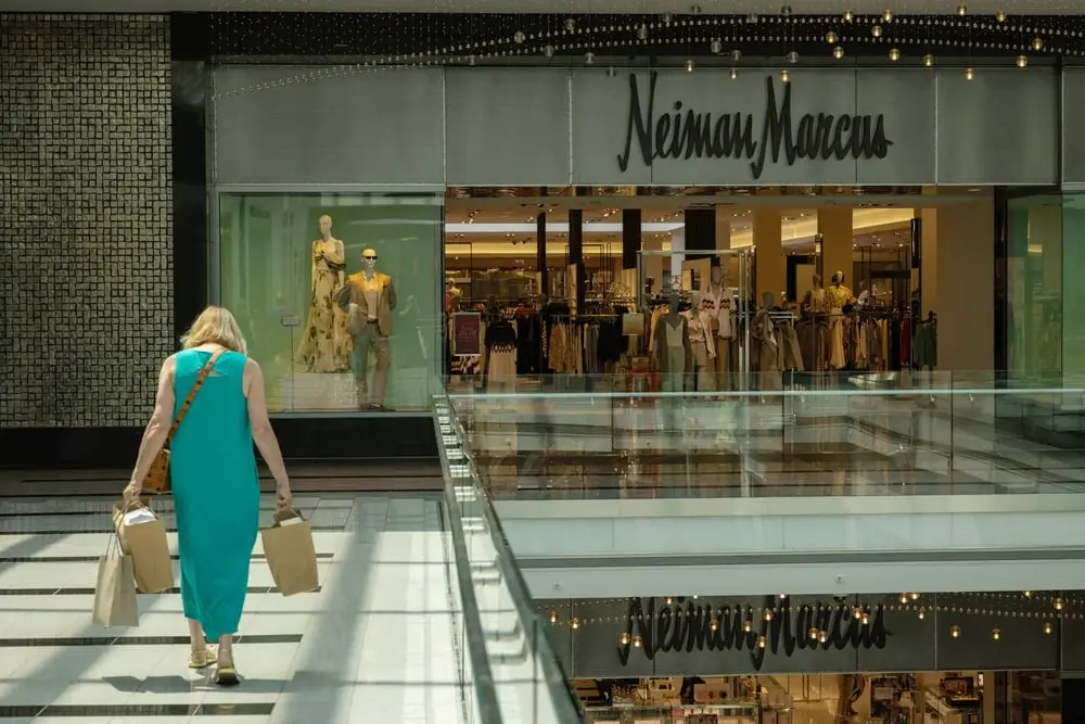 Une femme portant des sacs à provisions marche vers l'entrée d'un magasin Neiman Marcus dans un centre commercial.