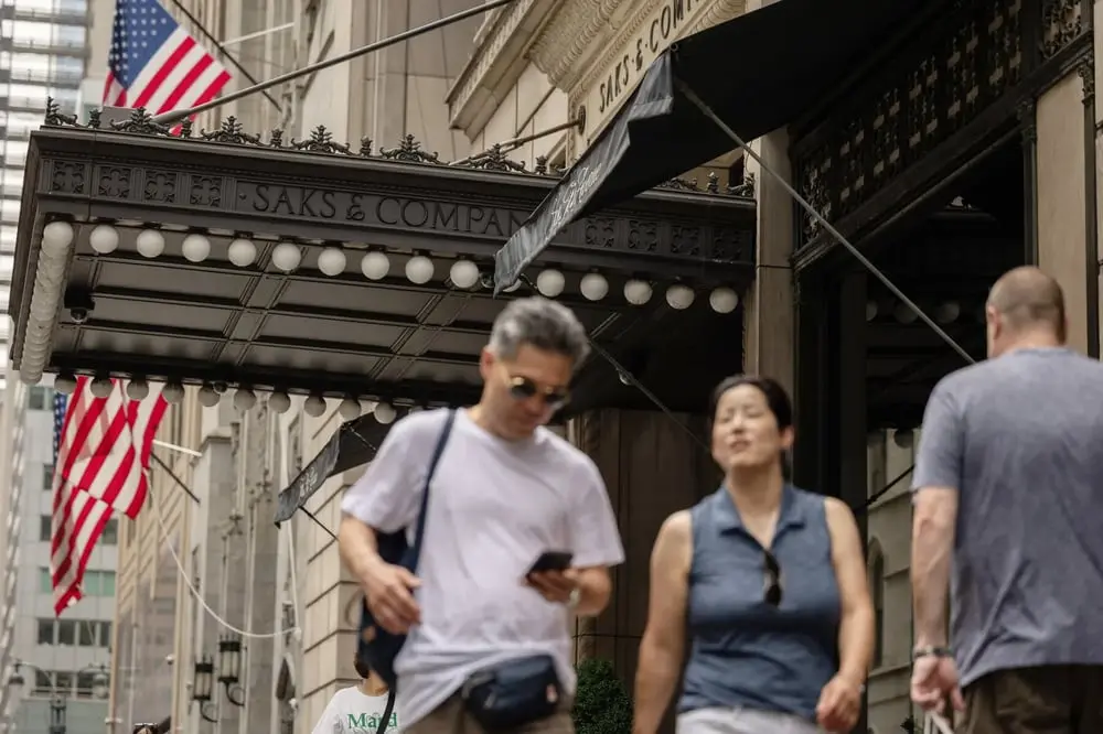 Passants devant l'entrée du magasin Saks & Company à côté de drapeaux américains flottants
