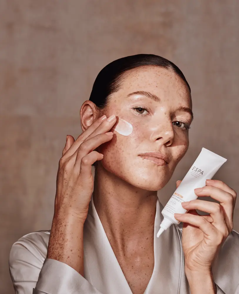 Une femme applique une crème ESPA sur son visage, illustrant la croissance de l'industrie Beauty de THG