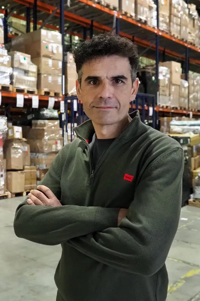 Homme debout dans un entrepôt de Tradeinn, entouré de cartons empilés sur des étagères métalliques